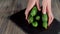 Summer salad. Woman puts several fresh juicy green cucumbers into the black board on a wooden table in focus of camera