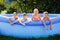 Summer season concept background. Four happy friends in an inflatable pool in the garden, refreshing themselves in hot weather