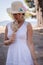 Summer Serenity: Barefoot Girl in White Dress with Straw Hat and Flowers by the Sea