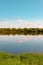 Summer sky with pink clouds reflecting in the water. Meadow and forest on the banks. Summer concept