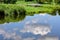 Summer sky and trees reflected in lake water