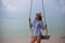 Summer solar portrait of fashion of a way of life of the young stylish woman,sitting on a swing on the beach,carrying lovely fashi