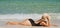 Summer sunbath. Vacation on beach. Woman in black swimwear lying on sandbeach. Girl near sea.