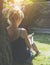 Summer sunny day. Back view. Young woman sits in a park under tree on a lawn and makes notes in a notebook.