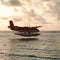 Summer sunset with seaplane. Landing seaplane on dawn seashore. Calm scenery on evening sea