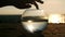 Summer sunset silhouette hand gently touches fishbowl with fish on beach