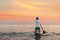 Summer surfing. Fit man swimming on a sup board. In the background, the ocean and the sunset sky. Sport and leisure