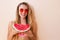 Summer taste. Cheerful young happy woman in swimsuit and sunglasses holding slice of watermelone standing outdoors