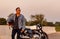 Summer travel on a motorcycle, motorcycle driver in black leather jacket stands on road with vintage motorcycle outstretched,