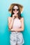 Summer travel woman in hat and sunglasses ready for feast trip and party isolated on blue background. Attractive smiling girl thin