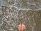 Summer vacation concept, woman feet toes in warm sea water and foam, pebbles beach