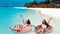 Summer Vacation. Enjoying suntan two women resting on donut float mattress in turquoise water on exotic beach. Maldives island