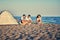 summer, vacation, holiday, happy people concept - friends relaxing with playing guitar and sing a song together on sea beach.