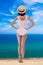 Summer vacation and travel concept - back view of giant young woman in swimsuit and straw hat standing on sea coast