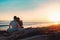 Summer vacation. A young couple posing against the sea, sitting on the rocks in an embrace. Rear view. Copy space. Sunset