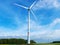 Summer view on huge white wind generators among green field and forest on blue sky and white clouds background. Wind energy techno