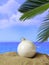 Summer xmas holidays concept. Christmas ball on sandy beach with palm tree, blue sea and sky background