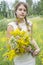 In the summertime  a girl is standing on the field and holding a bouquet of yellow wildflowers