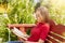 Summertime and leisure concept. Sideways portrait of attractive schoolgirl wearing red sweater reading attentively book preparing