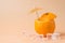 Summertime relax concept. Close-up photo of cut orange with a cocktail umbrella in it and ice cubes isolated on sandy background