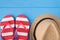 Summertime relax concept. Top above overhead view photo of striped flipflops and hat isolated on blue wooden background