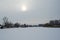 Sun on the background of a winter gray sky and the frozen river