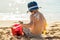 The sun drawing sunscreen ,suntan lotion on baby boy back. Caucasian child is sitting with plastic container of sunscreen and toys