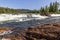 A sun-drenched summer day reveals the Namsen River in Namsskogan, Norway, cascading over rocks with solitary trees