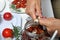 Sun-dried tomatoes with spices and garlic in a jar. Woman adds garlic. Near rosemary, tomatoes and garlic