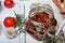 Sun-dried tomatoes with spices and garlic in a jar. Woman adds ingredients. Near rosemary, tomatoes and garlic