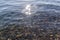 Sun glare and colorful  pebbles in the silver clear blue water of lake baikal, ripples, shore