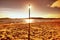 Sun hidden behind blue pole on sandy beach at sea. Forest hill on island in background