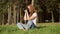 Sun-kissed freckled redhead girl with photo-camera is sitting on a green grass and takes a photo.