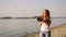 Sun-kissed freckled redhead girl with photo-camera is walking on bank of river.