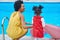 Sun-Kissed Smiles: Afro-American Mother and Daughter Embrace Poolside Joy in Vibrant Dresses