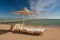 Sun lounger under the beach umbrella with view at the sea coast. Blue sky and white clouds over a resort beach.