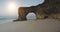 Sun natural arch hole in cliff wall at ocean coast closeup aerial. Tourist attraction on sand beach