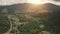 Sun over green mountain village slow motion aerial. Summer nature landscape. Cottages at rural road