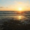 Sun over horizon and  rolling ocean waves to the shore while sunset during tide.  Beautiful seascape of a sandy beach  with green
