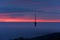 The sun is rising behind the tv tower and the clouds