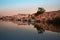 The sun is rising at the port of Mazara del Vallo in Sicily. The sky is reflected in the water. Houses line the harbor edge and