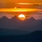 Sun sets dramatically behind silhouetted peaks, painting sky golden