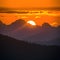 Sun sets dramatically behind silhouetted peaks, painting sky golden