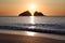 The sun sets in the middle the V shape of the Gull Rocks at Holywell Bay in Cornwall