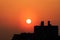 Sun sets through orange haze over silhouetted buildings