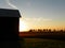 Sun setting behind barn and fields of corn in the autumn countryside