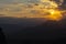 Sun setting behind dramatic clouds and beyond dark silhouette mountains