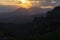 Sun setting behind dramatic clouds and beyond dark silhouette mountains