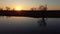 Sun setting behind levee on river with tractor and reflection on water