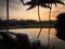 Sun setting behind silhouetted palms and reflections on infinity pool and golf course in Hawaii